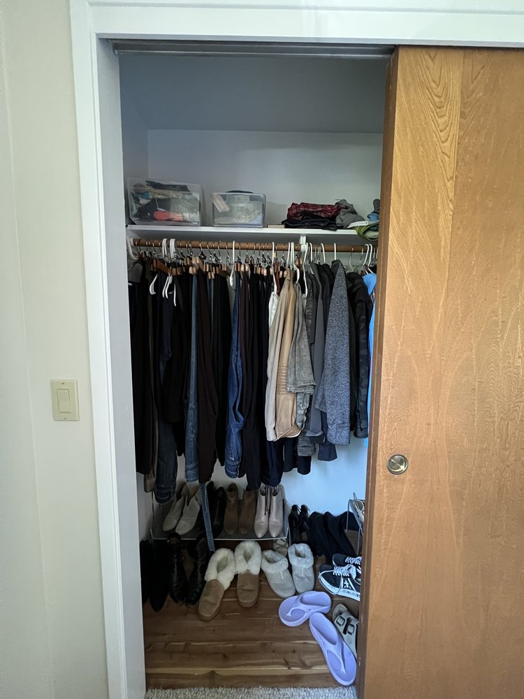 Cluttered bedroom closet with hanging clothes in disarray and shoes scattered on floor