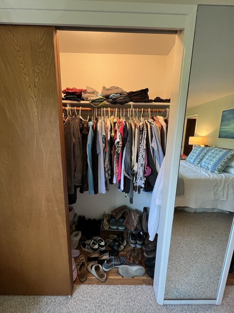 Overstuffed reach-in closet with clothes crammed together and items scattered on shelves
