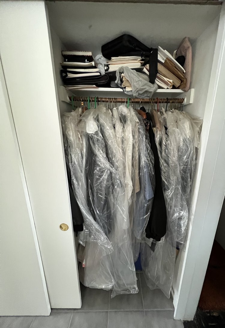 Messy reach-in closet with clothes still in dry-cleaning bags and no visible organization system