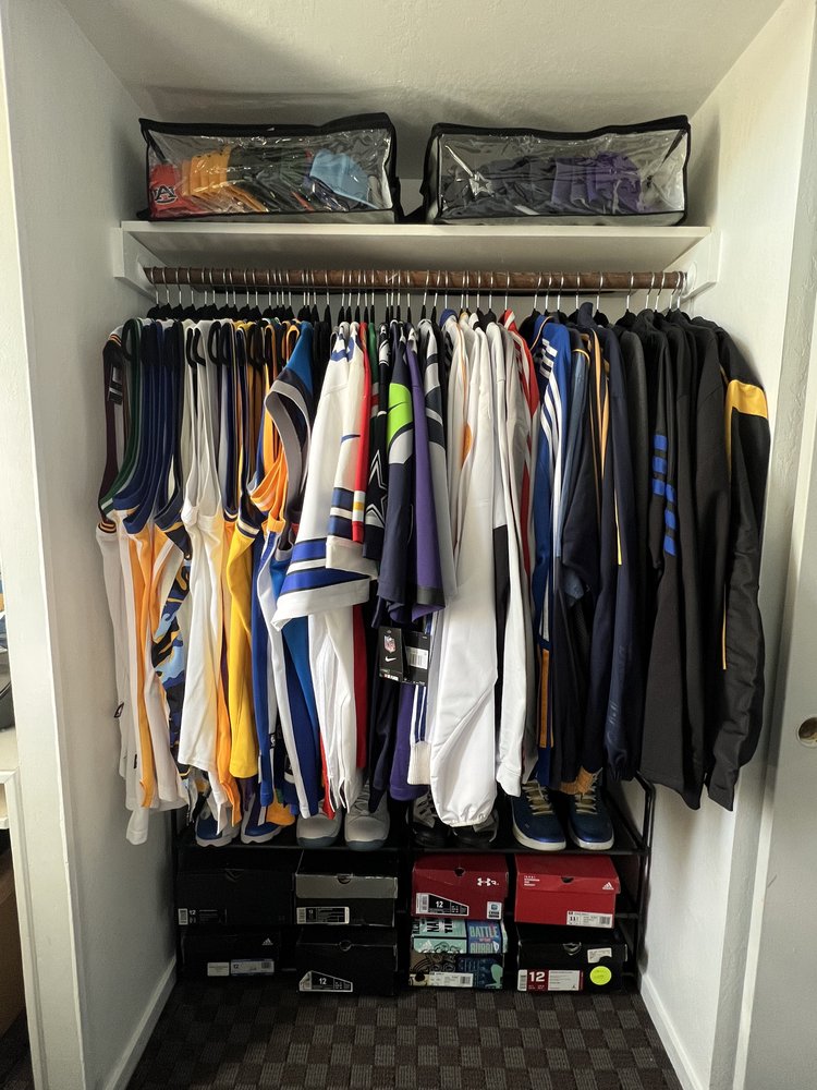 Organized sports apparel closet with jerseys hung neatly, sneakers arranged on shoe rack, and hats systematically stored