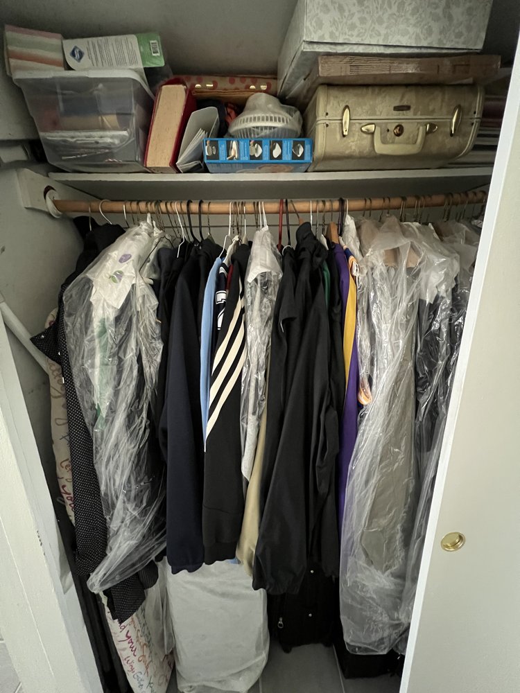 Overcrowded reach-in hall closet with seasonal clothes mixed together and storage items stacked high